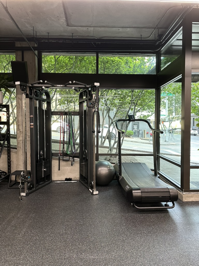 Functional trainer and treadmill beside floor-to-ceiling windows looking onto Cedar St in Belltown